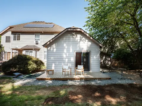 A white backyard ADU with a small deck, behind the main house